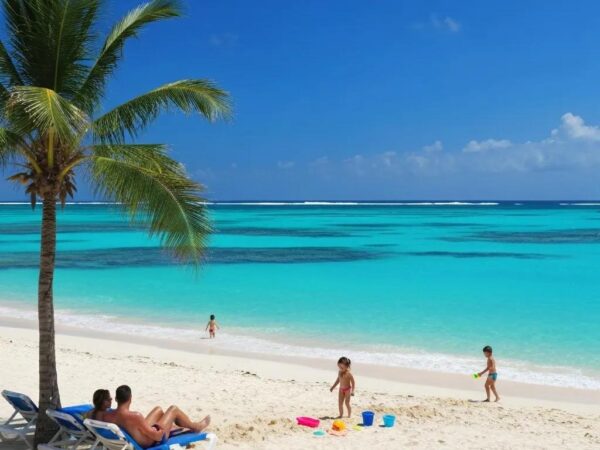 Familia disfrutando de la playa en Punta Cana, con aguas turquesas y palmera, representando un destino atractivo para inversiones en bienes raíces.